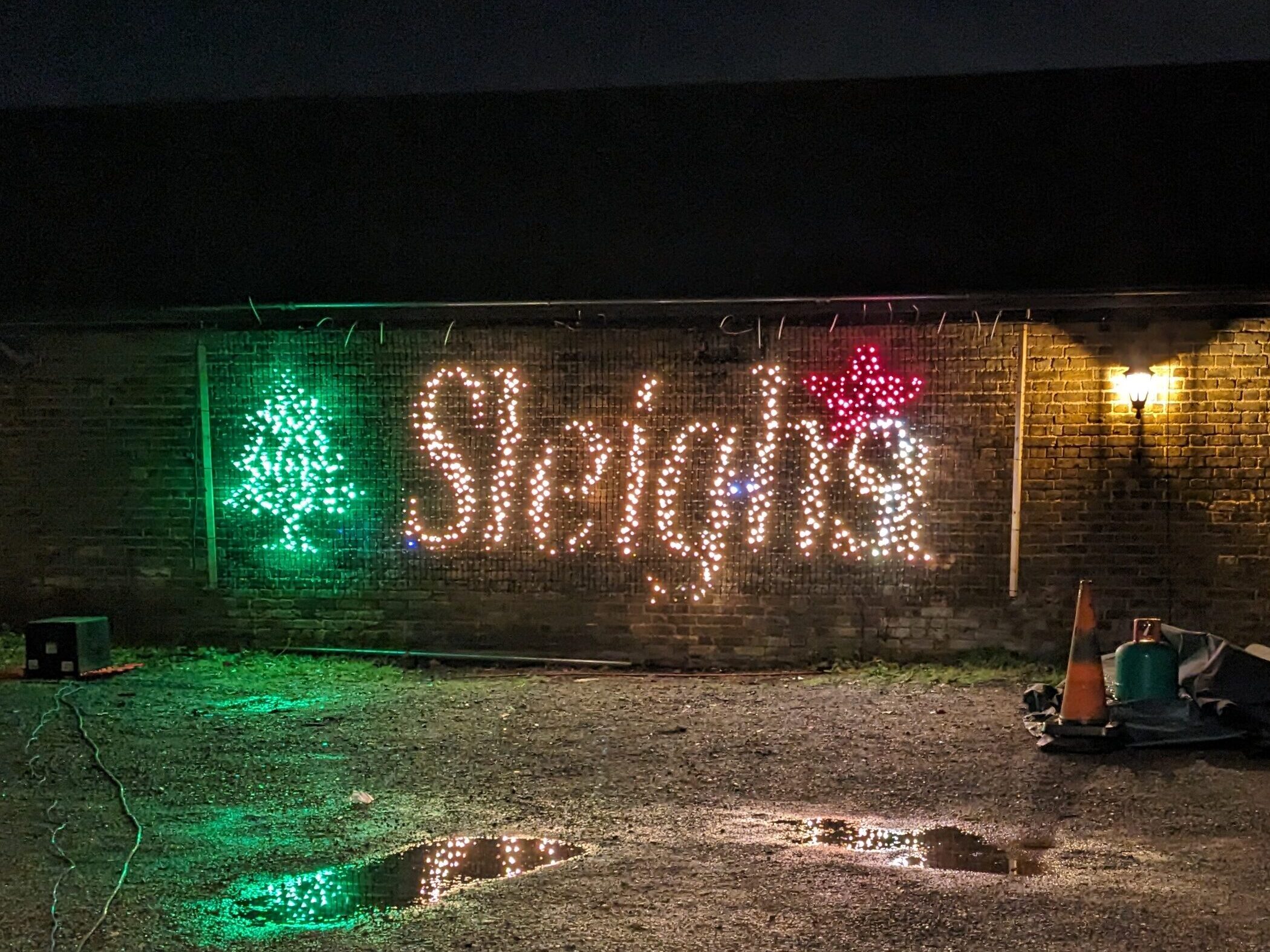 a christmas display with the word 'Sleighs' suspended to a wall with a puddle in front