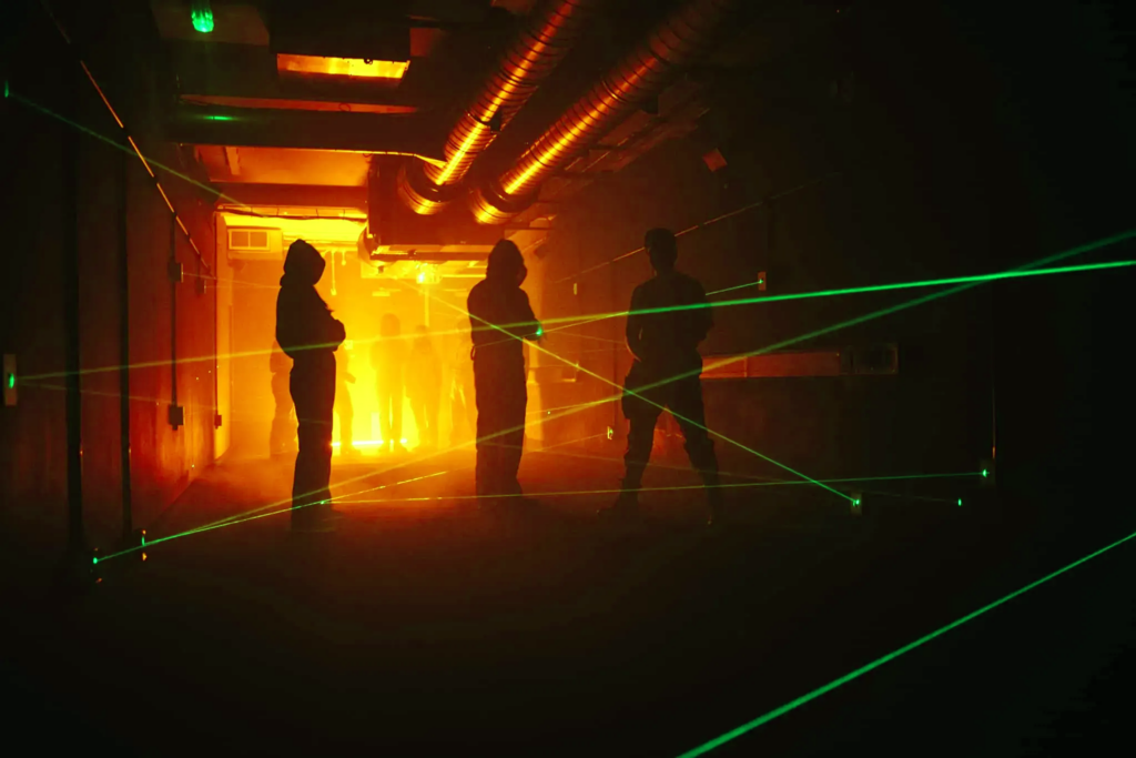 silhoutettes of people making their way through a laser laze. green laser beams show in the foreground.